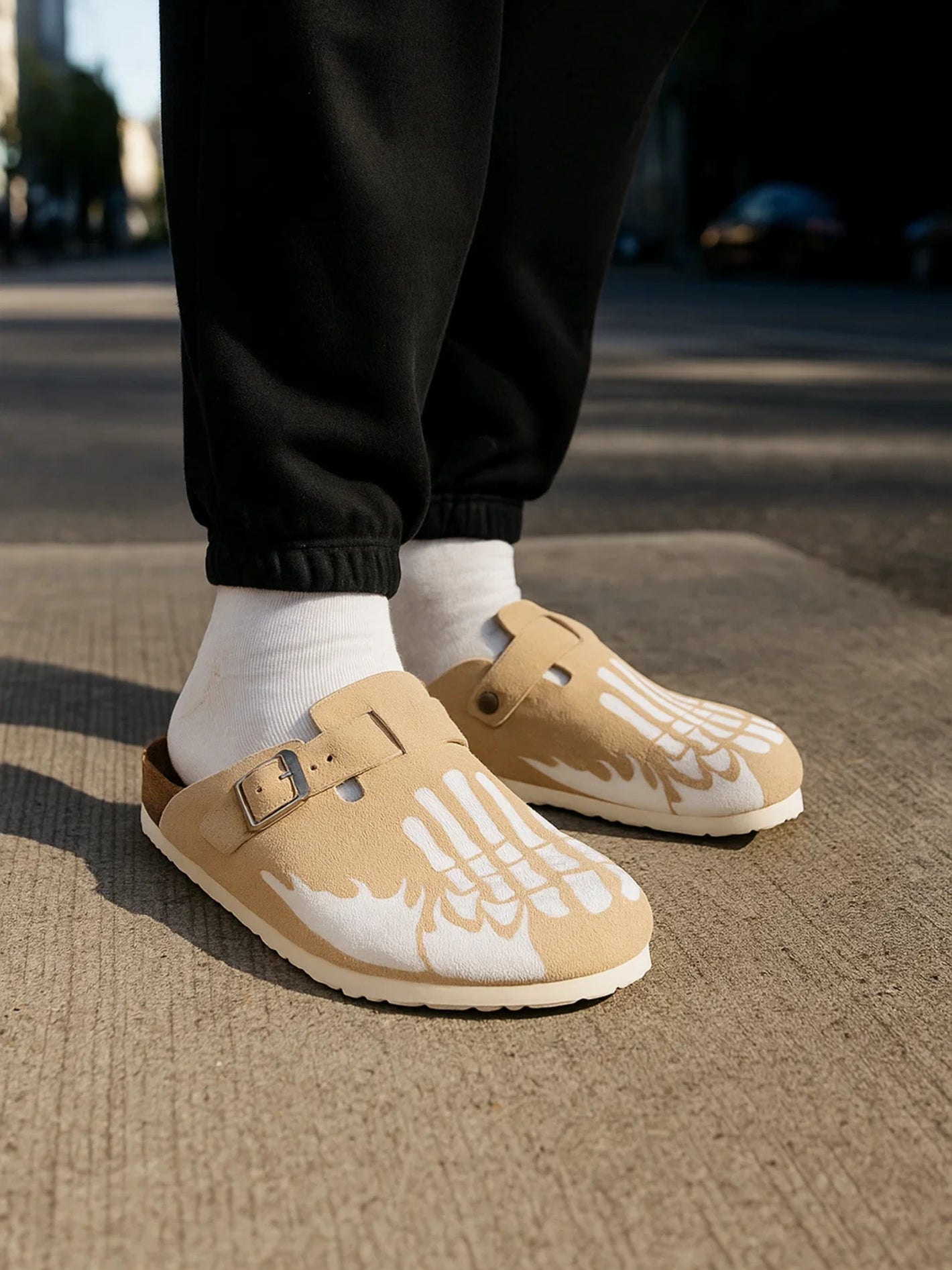 Beige clogs worn with black pants and white socks on a street.