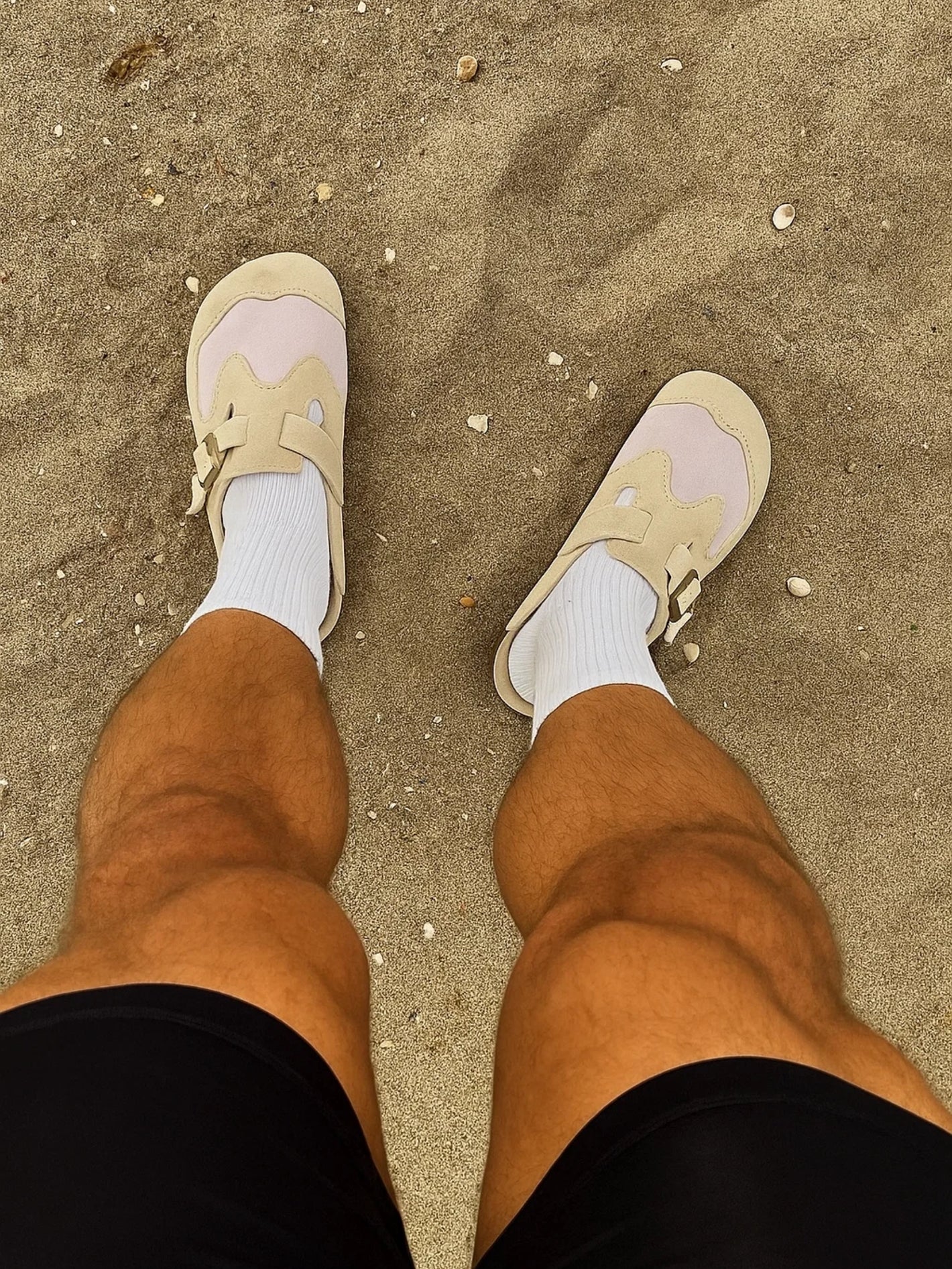 Beige sneakers and brown pants on a sandy surface